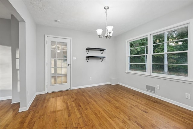 unfurnished dining area with an inviting chandelier, wood-type flooring, and a textured ceiling