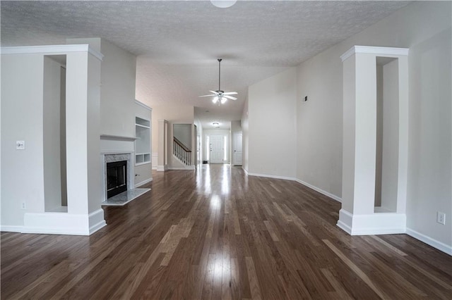 unfurnished living room featuring ceiling fan, dark wood-type flooring, a fireplace, built in features, and a textured ceiling