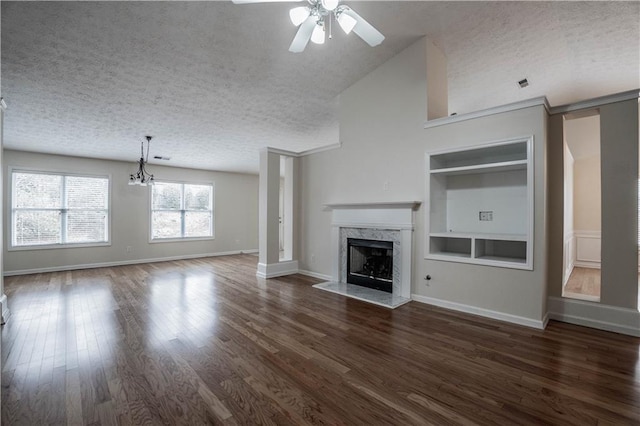 unfurnished living room featuring ceiling fan with notable chandelier, a textured ceiling, dark hardwood / wood-style flooring, a premium fireplace, and built in features