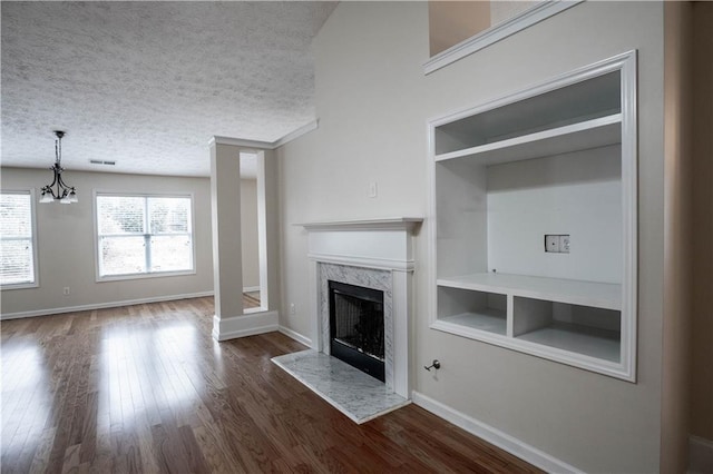 unfurnished living room with a textured ceiling, a high end fireplace, built in shelves, dark hardwood / wood-style floors, and a chandelier