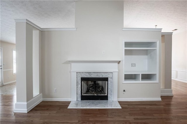 unfurnished living room featuring a premium fireplace, dark hardwood / wood-style flooring, built in features, a textured ceiling, and crown molding