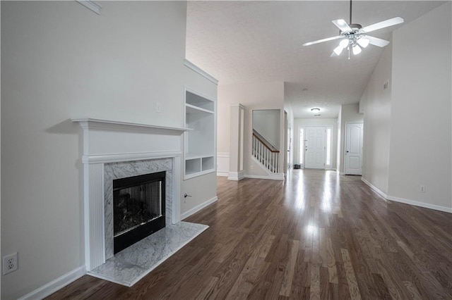 unfurnished living room with a premium fireplace, built in features, dark hardwood / wood-style floors, and ceiling fan