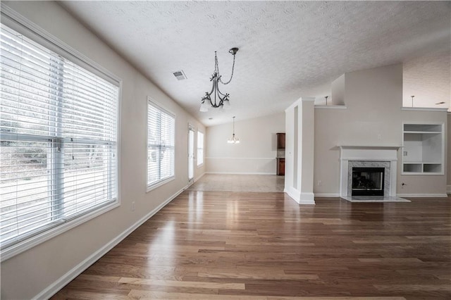 unfurnished living room featuring a textured ceiling, a high end fireplace, lofted ceiling, dark hardwood / wood-style flooring, and an inviting chandelier