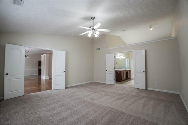 unfurnished bedroom with ceiling fan, connected bathroom, light carpet, and lofted ceiling