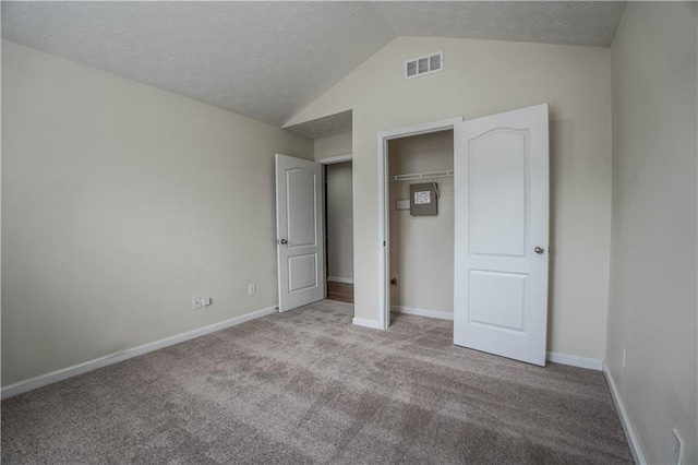 unfurnished bedroom featuring a textured ceiling, lofted ceiling, a closet, and light carpet