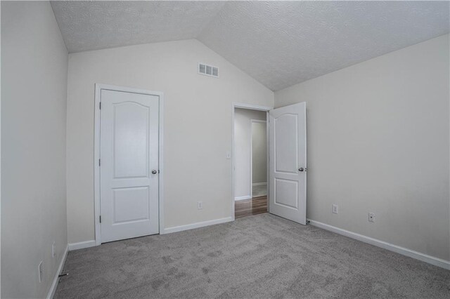 unfurnished bedroom with a textured ceiling, vaulted ceiling, and light carpet