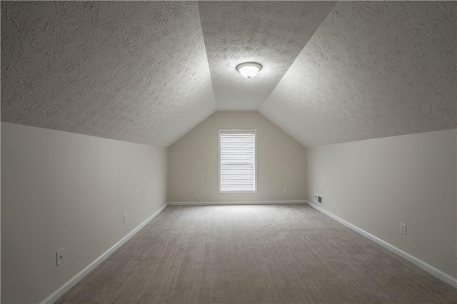 additional living space featuring a textured ceiling, lofted ceiling, and carpet flooring