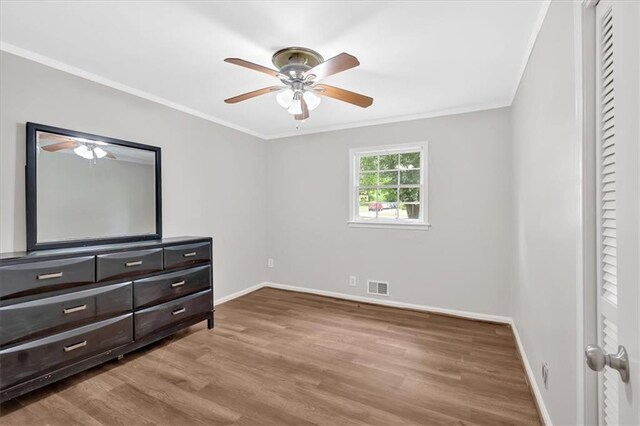 unfurnished bedroom featuring wood finished floors, crown molding, baseboards, and a ceiling fan