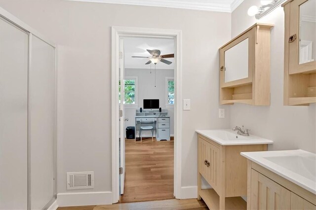 full bathroom featuring a ceiling fan, wood finished floors, two vanities, crown molding, and baseboards