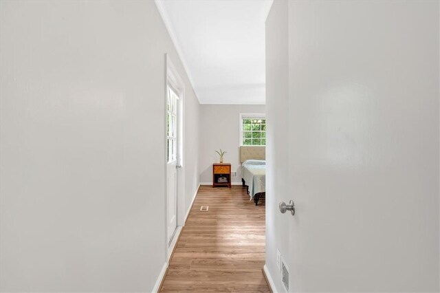 hallway featuring light wood-style floors, ornamental molding, and baseboards