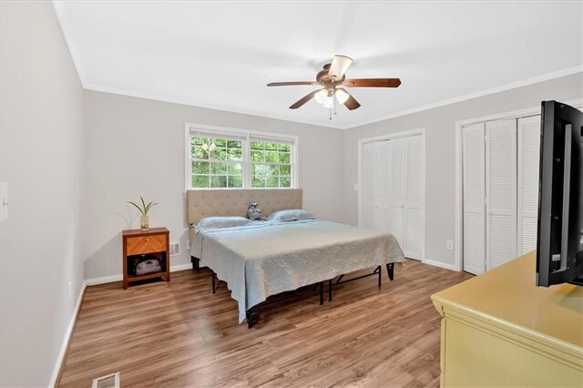 bedroom featuring two closets, baseboards, crown molding, light wood-style flooring, and ceiling fan