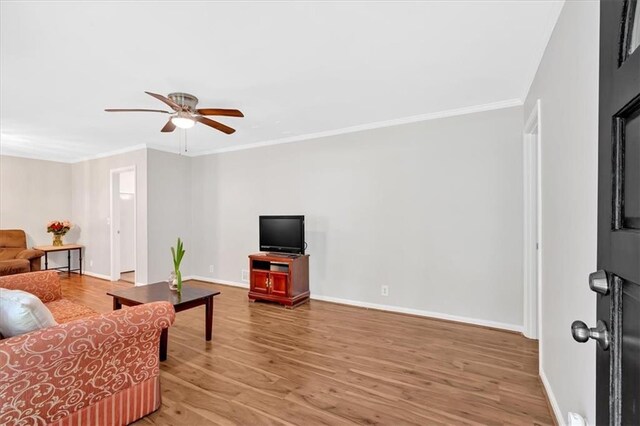 living area featuring ceiling fan, light wood-style flooring, baseboards, and crown molding