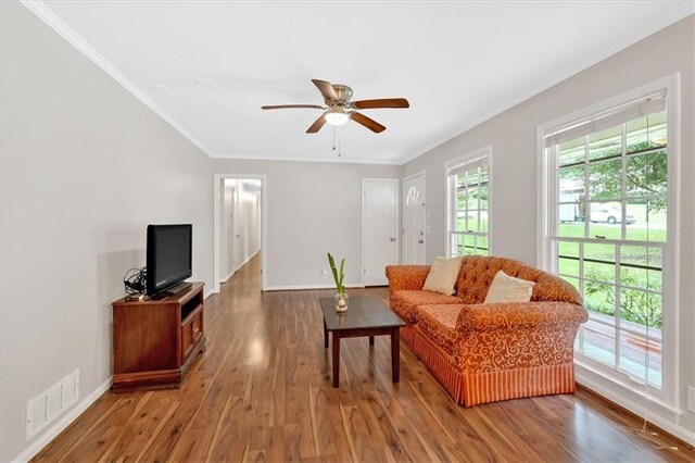 living area with wood finished floors, crown molding, ceiling fan, and baseboards