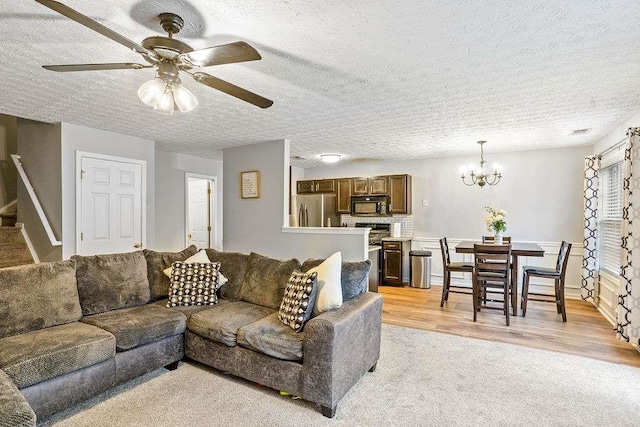 living room with ceiling fan with notable chandelier, a textured ceiling, and light wood-type flooring