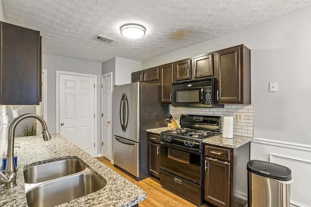 kitchen with sink, light hardwood / wood-style flooring, light stone counters, dark brown cabinetry, and black appliances