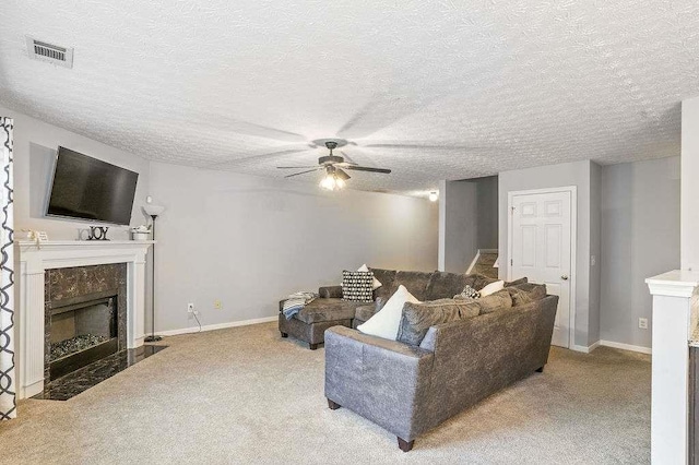 living room featuring ceiling fan, a high end fireplace, light carpet, and a textured ceiling