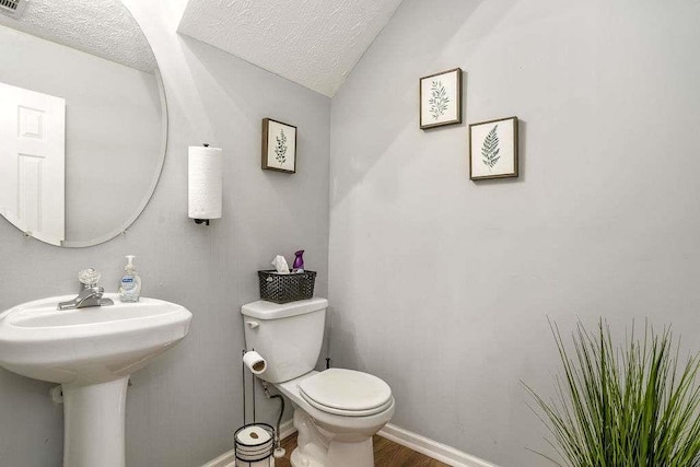 bathroom featuring hardwood / wood-style flooring, lofted ceiling, toilet, and a textured ceiling