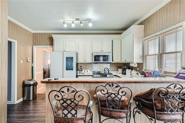 kitchen featuring a peninsula, ornamental molding, freestanding refrigerator, stainless steel microwave, and dark wood finished floors