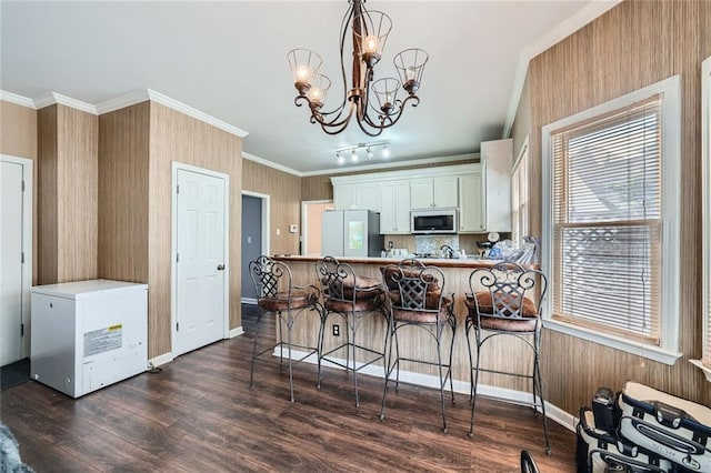 kitchen with a breakfast bar area, crown molding, freestanding refrigerator, dark wood-style floors, and an inviting chandelier