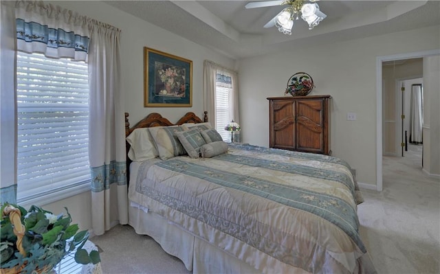 bedroom featuring a tray ceiling, light carpet, ceiling fan, and ensuite bath