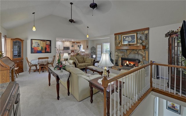carpeted living room featuring a stone fireplace, high vaulted ceiling, and ceiling fan