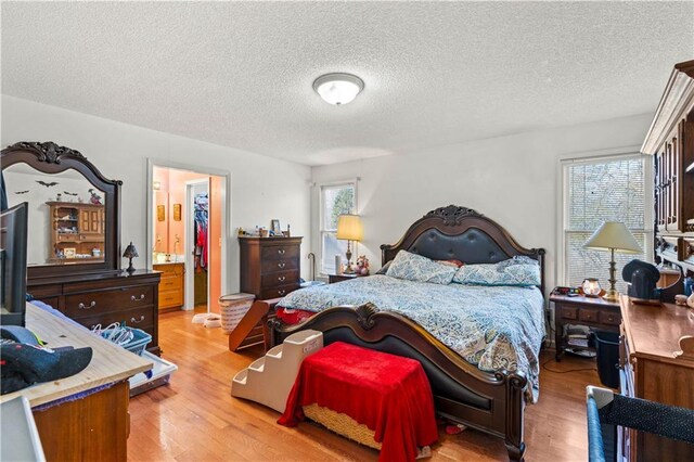 bedroom with wood-type flooring, connected bathroom, multiple windows, and a textured ceiling