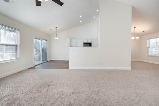 unfurnished living room with carpet, ceiling fan with notable chandelier, and high vaulted ceiling