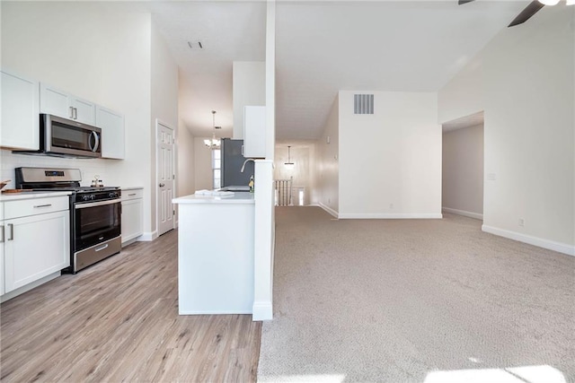 kitchen with a high ceiling, ceiling fan with notable chandelier, light colored carpet, white cabinetry, and stainless steel appliances