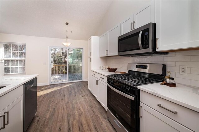 kitchen with appliances with stainless steel finishes, white cabinetry, lofted ceiling, and light stone counters