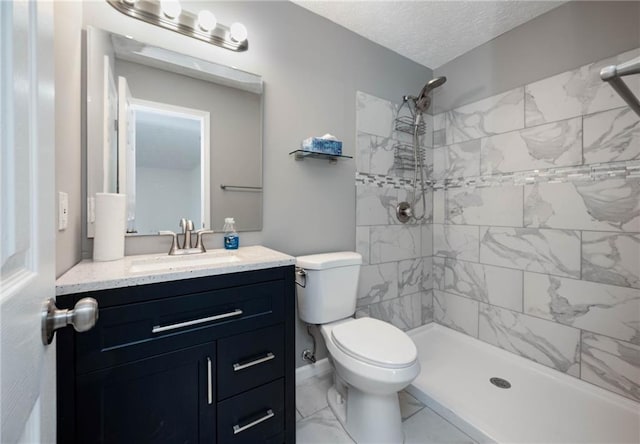 bathroom featuring vanity, toilet, tiled shower, and a textured ceiling