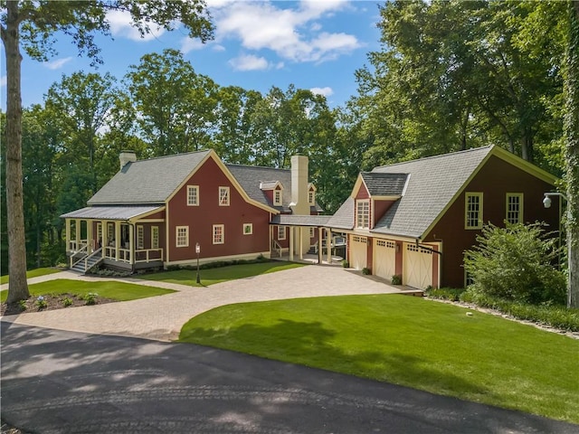 view of front facade featuring a front lawn, a porch, a chimney, a garage, and driveway