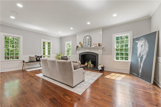 living area with a wealth of natural light, a brick fireplace, hardwood / wood-style floors, and ornamental molding