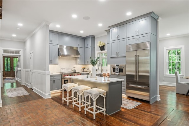 kitchen featuring premium appliances, crown molding, gray cabinets, and wall chimney range hood