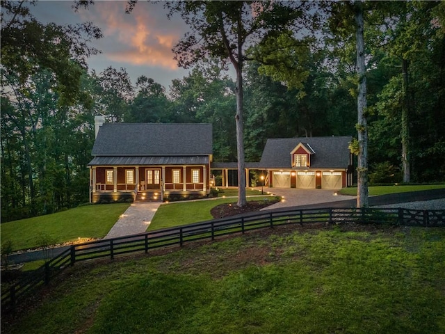 rear view of property with a porch, a yard, curved driveway, a garage, and a fenced front yard