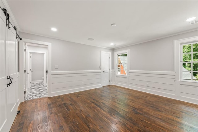 spare room featuring dark hardwood / wood-style flooring, ornamental molding, and a barn door