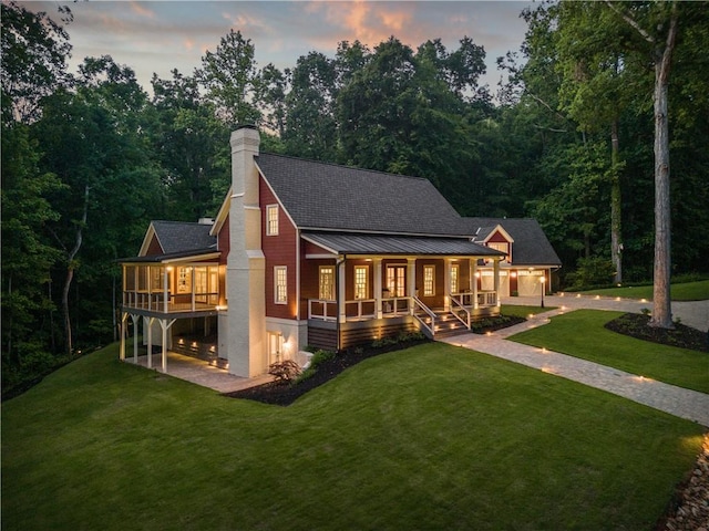 back of house at dusk featuring covered porch, a patio, a chimney, and a yard