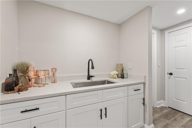 kitchen with white cabinetry, wood finished floors, light countertops, and a sink