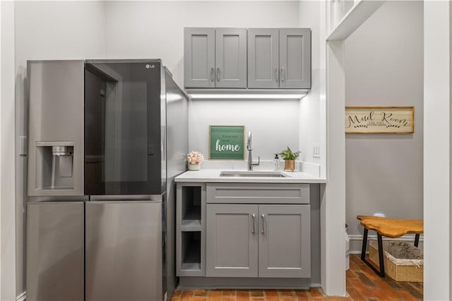 kitchen featuring brick floor, gray cabinets, a sink, light countertops, and stainless steel fridge