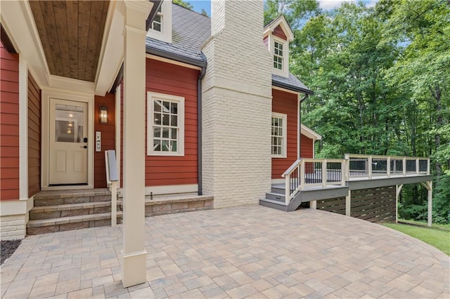 entrance to property featuring a wooden deck, a chimney, a patio, and brick siding