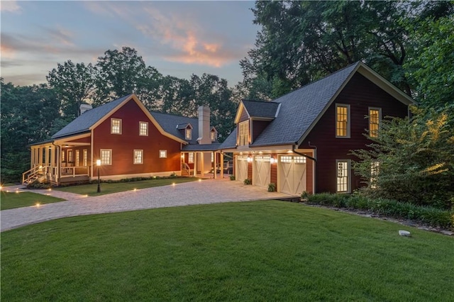 back house at dusk featuring a garage and a lawn