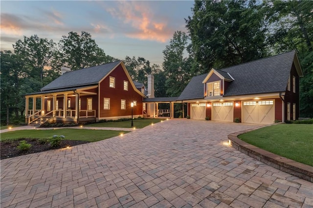 view of front of property with a front yard, driveway, a porch, an attached garage, and a chimney