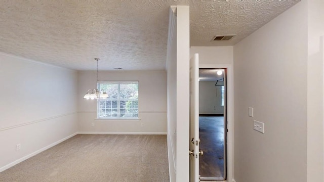 empty room with a textured ceiling, baseboards, a chandelier, and carpet