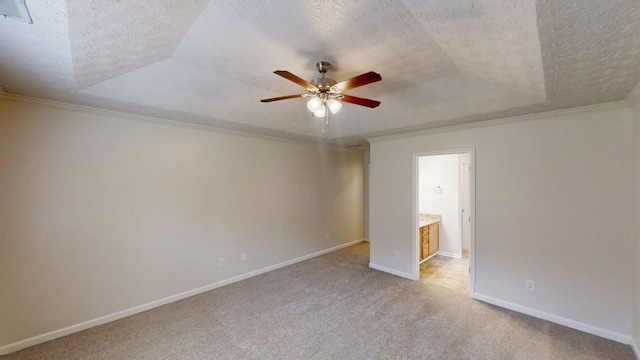 carpeted spare room featuring a textured ceiling, ceiling fan, a raised ceiling, baseboards, and ornamental molding
