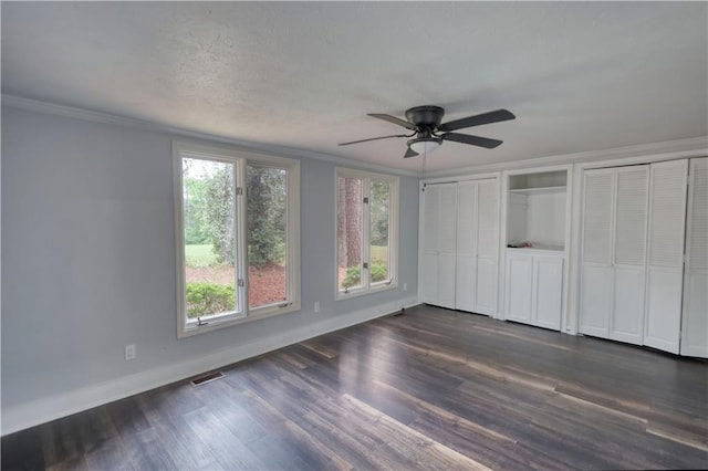 unfurnished bedroom featuring baseboards, ornamental molding, dark wood-type flooring, two closets, and a ceiling fan