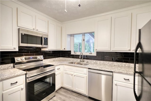 kitchen with appliances with stainless steel finishes, a sink, white cabinetry, backsplash, and crown molding