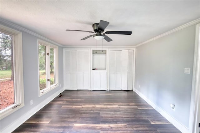 unfurnished bedroom with two closets, multiple windows, baseboards, dark wood finished floors, and ornamental molding