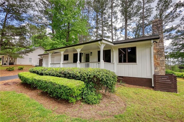 view of front of house featuring a porch, a chimney, board and batten siding, and a front lawn