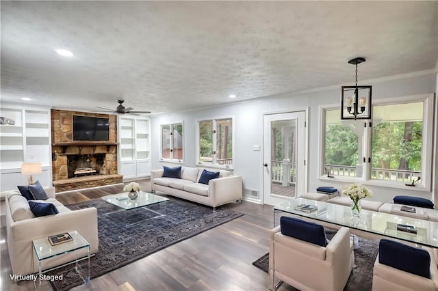 living room featuring a chandelier, plenty of natural light, wood finished floors, ornamental molding, and a stone fireplace