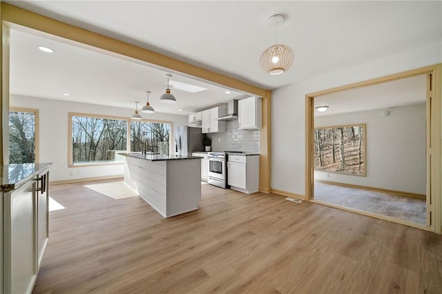 kitchen with decorative backsplash, light wood-style flooring, stainless steel appliances, wall chimney range hood, and white cabinetry