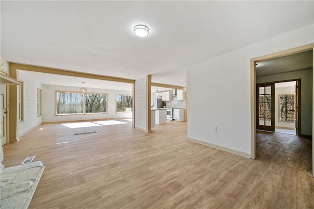 unfurnished living room with light wood-type flooring, visible vents, and baseboards